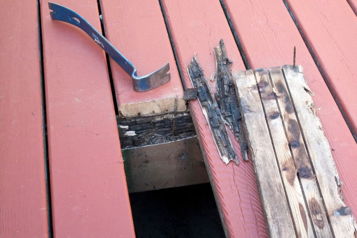 A wooden deck featuring a pry-bar resting on a wooden plank, showing a removed rotten deck board.