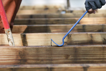 A person uses a blue crowbar to remove nails from wooden planks. The focus is on the tool and wood, conveying a theme of construction or renovation.