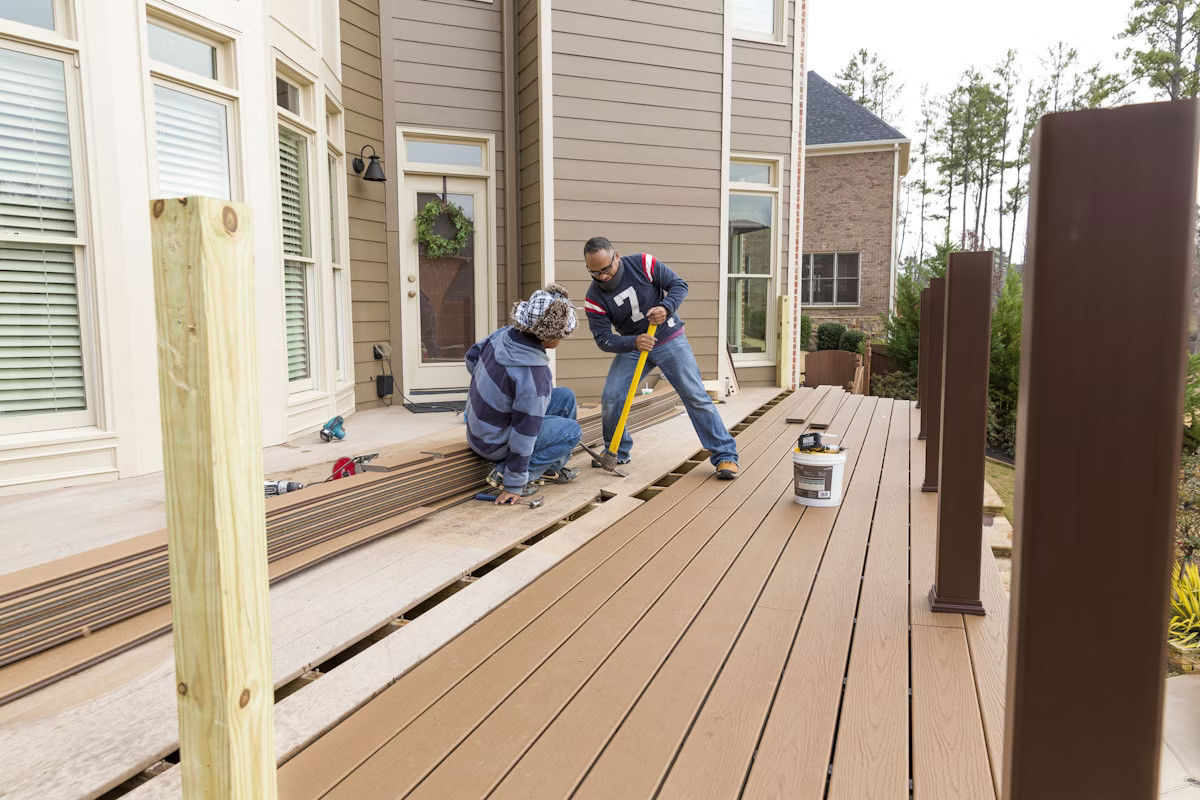 Two men collaborating on replacing the boards on a deck, with a wooden railing in progress.