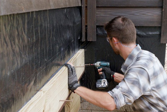 Contractor fastening a ledger board to a house.