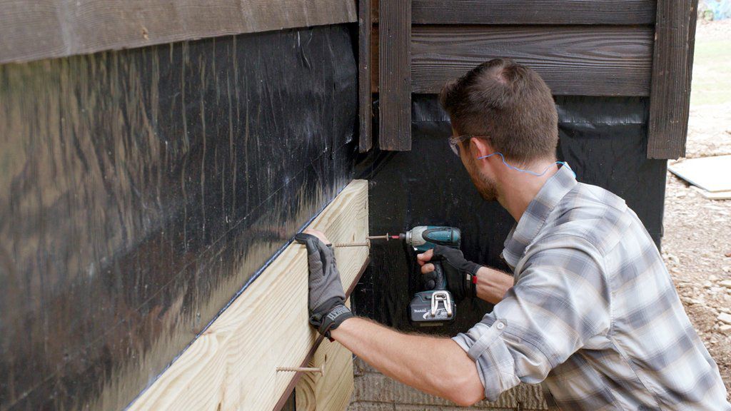 Contractor fastening a ledger board to a house.