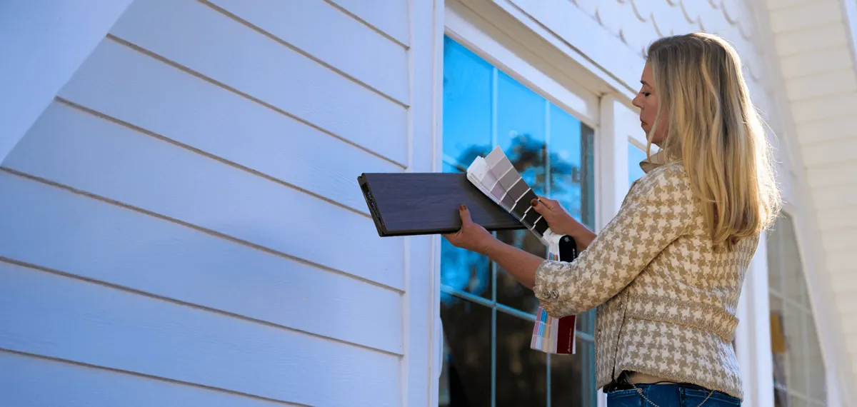 Person Comparing Color Swatches To Composite Deck Board And House